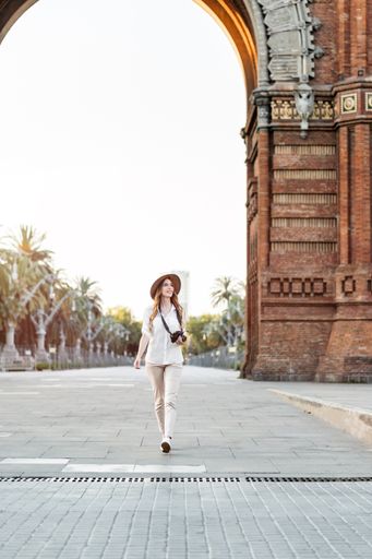 A young female tourist with a fedora hat and a camera walking down the Barcelona streets in Spain