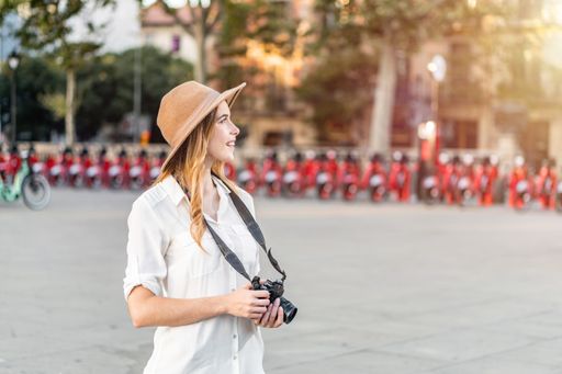 A shallow focus of a young female tourist with a fedora hat holding a camera in Barcelona, Spain