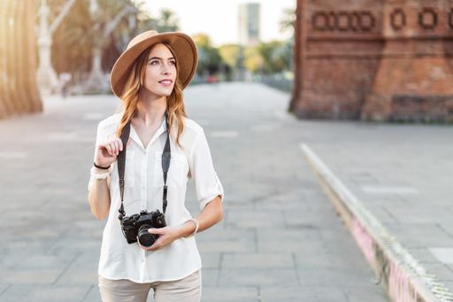A shallow focus of a young female tourist with a fedora hat holding a camera in Barcelona, Spain