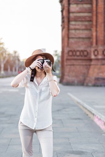 A shallow focus of a young female tourist with a fedora hat taking pictures in Barcelona, Spain