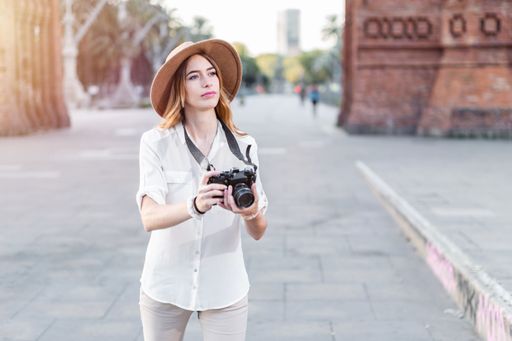 A shallow focus of a young female tourist with a fedora hat and a camera in Barcelona, Spain