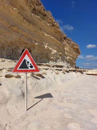 A vertical shot of a warning road sign next to limestone rocks