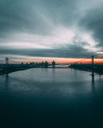 The Ambassador Bridge in Michigan on a river surrounded by a town under a cloudy sky during sunset