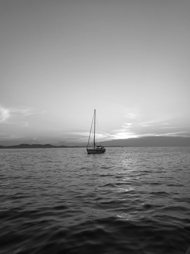 A vertical shot of a sailboat at sea in grayscale