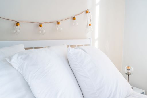 The fairy bulb lights hanging on top of a bed with white pillows.