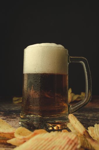 A vertical shot of a cold beer with foam on a table with chips