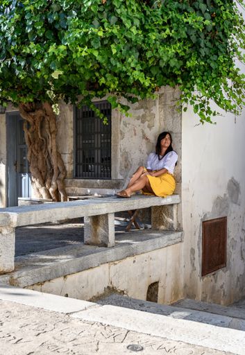 a vertical shot of a white caucasian woman lying on the stone bench under a tree