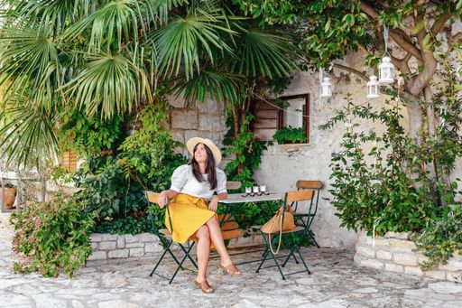 a white caucasian woman sitting on an outdoor chair under a tree and looking up