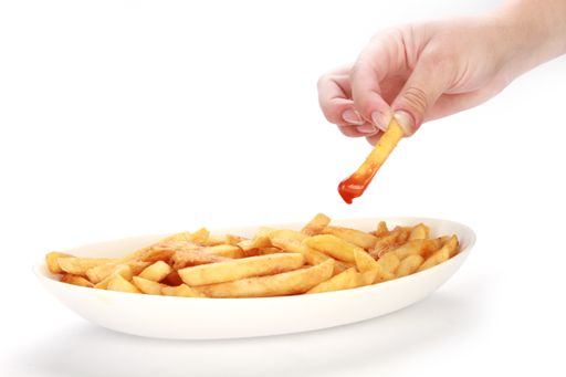 A man's hand picking a piece of french fries with catsup isolated on white background