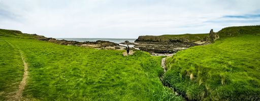 A panoramic of a person walking on green hills of Northern Ireland, and the North Atlantic Ocean on the horizon