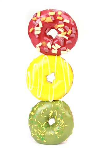 A vertical shot of three colorful glazed doughnuts isolated on white background