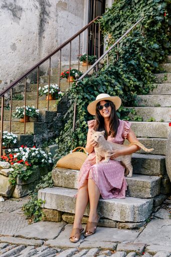 a vertical shot of a white caucasian woman with an orange striped cat sitting on the stairs