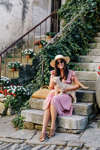 a vertical shot of a white caucasian woman with an orange striped cat sitting on the stairs