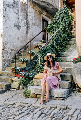 a vertical shot of a white caucasian woman with an orange striped cat sitting on the stairs