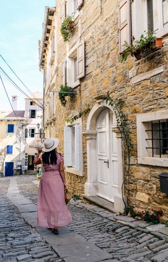 a vertical shot of a  woman with a pink dress walking down the road next to a building