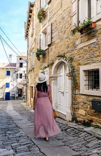 a vertical shot of a  woman with a pink dress walking down the road next to a building