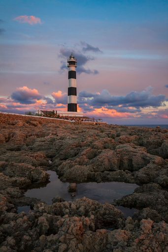 A vertical shot of a lighthouse against a cloudy sky during the sunset
