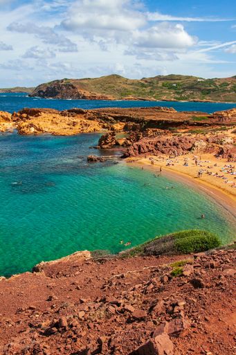Many tourists resting on a sandy beach and swimming in a sea with crystal water on a sunny day