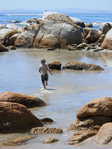 A vertical shot of a Caucasian boy running on a rocky beach on the West Coast of South Africa