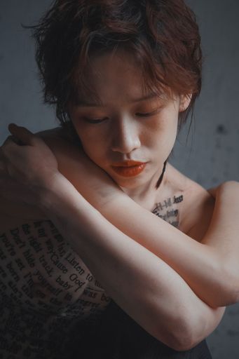 A portrait of a sad pretty East Asian female with short hair and english text on her body