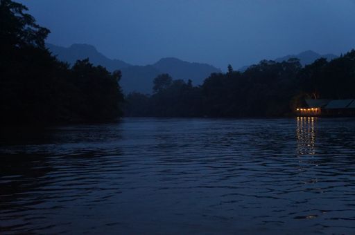 A night view of a peaceful lake surrounded by a forest with a lighted house on the side