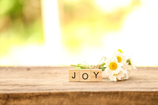 A top view shot of wooden blocks spelled joy with white daisy flowers on a wooden surface