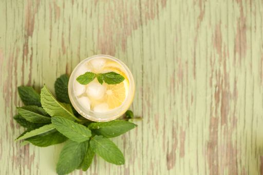 A refreshing summer drink with fresh lemon slices and mint leaves on a wooden green background