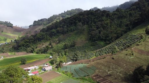 A high-angle shot over a small village surrounded by a mountainous landscape and clouds in the sky