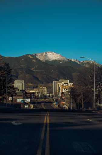 A vertical shot of a road near buildings and mountains under a blue sky in Colorado Springs