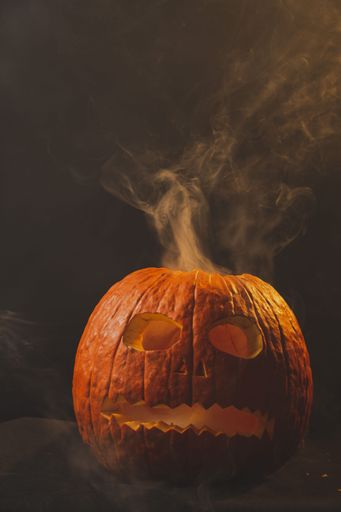 A vertical shot of a jack-o-lantern made of a pumpkin with smoke coming out of its head
