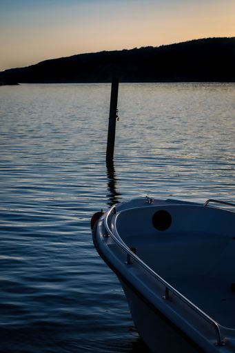 A vertical shot of a docked boat with silhouette view of a cliff in the background at sunset