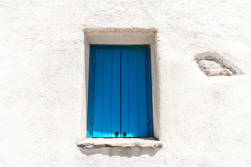 A small window with blue shutters on a white building wall. Greece.