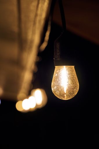 A vertical shot of a turned-on light bulb hanging on the ceiling in the darkness