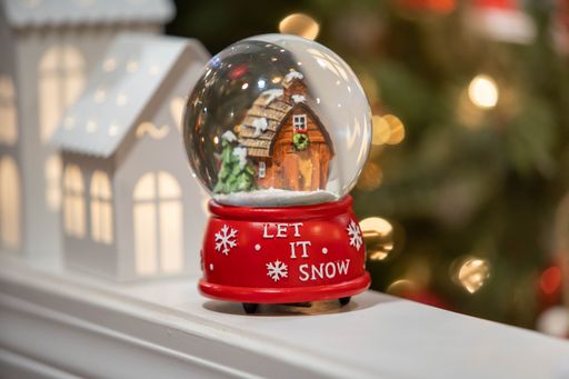 A small Christmas snow globe with a "Let it snow" text on it on the blurred background