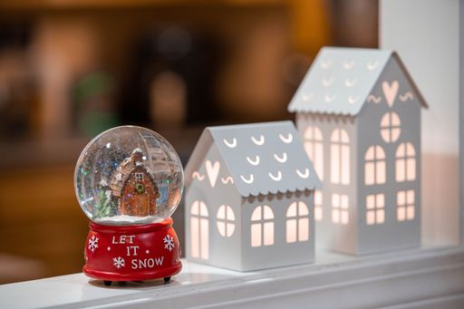A small Christmas snow globe with a "Let it snow" text on it on the blurred background