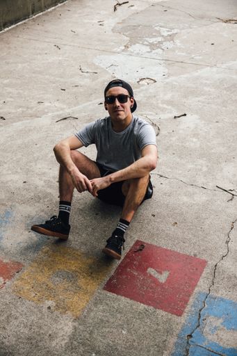 A vertical shot of a cool young man wearing a hat and sunglasses sitting on the ground