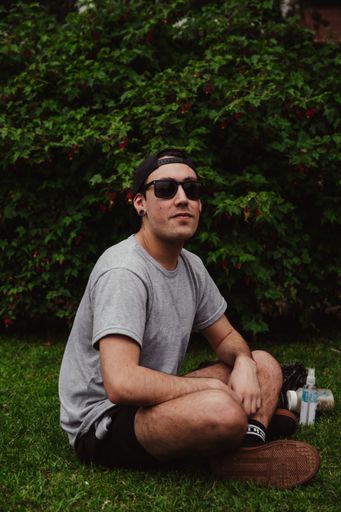 A vertical shot of a stylish young man sitting on the grass