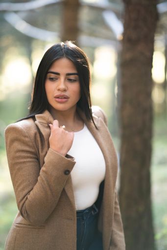 A selective focus shot  of a stylish brunette woman in a brown coat in a forest - autumn mood