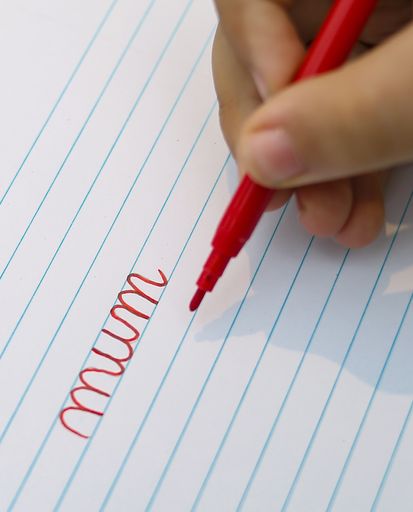 A child writes the word mom in a school notebook.