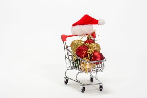 A vertical shot of a small shopping cart filled with Christmas ornaments on a white surface