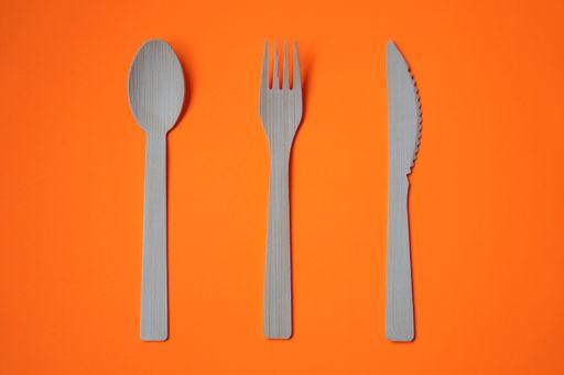 A closeup of a set of spoon, knife, and fork on an orange surface