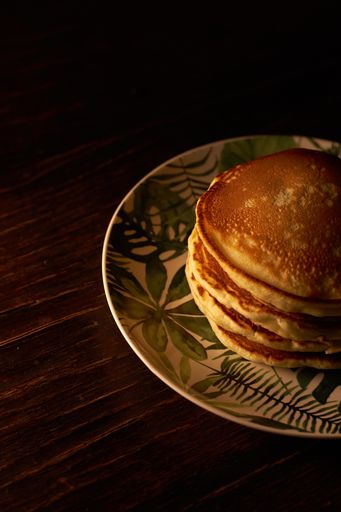 A vertical shot of a stack of freshly baked pancakes in a white plate on a wooden surface