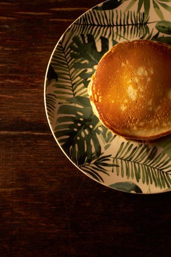 A vertical shot of a stack of freshly baked pancakes in a white plate on a wooden surface