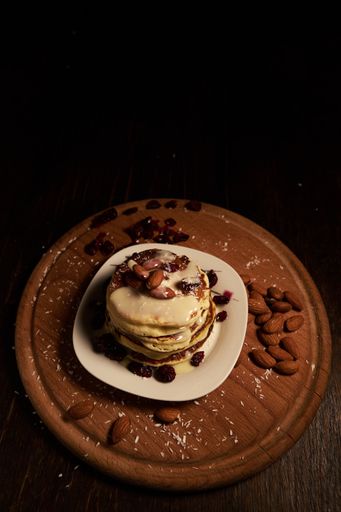 A vertical high angle shot of a stack of pancakes with white syrup and almonds on top on a wooden tray covered with baking powder