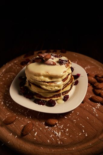 A vertical high angle shot of a stack of pancakes with white syrup and almonds on top on a wooden tray covered with baking powder