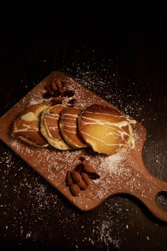 A vertical high angle shot of freshly baked pancakes with white syrup and almonds covered with coconut powder on a wooden surface