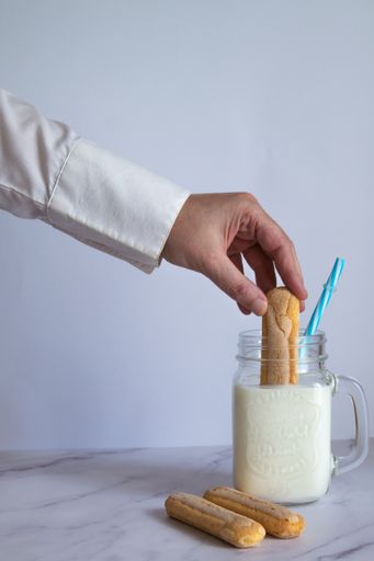 A vertical shot of male hand dipping cookie on a milkshake