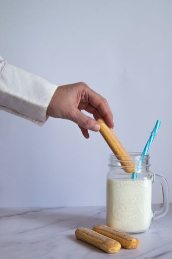 A vertical shot of male hand dipping cookie on a milkshake