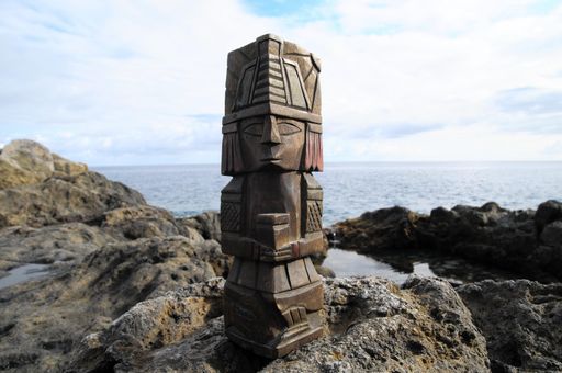 A closeup of an ancient Maya statue standing on the rock in front of the beach on a sunny day