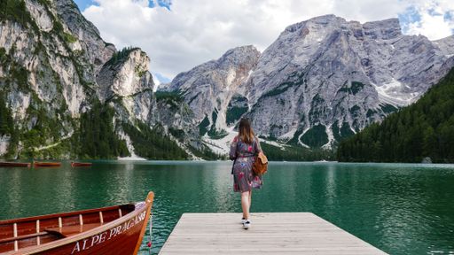 A young Caucasian female standing on a cliff by a lake surrounded by rocky mountains